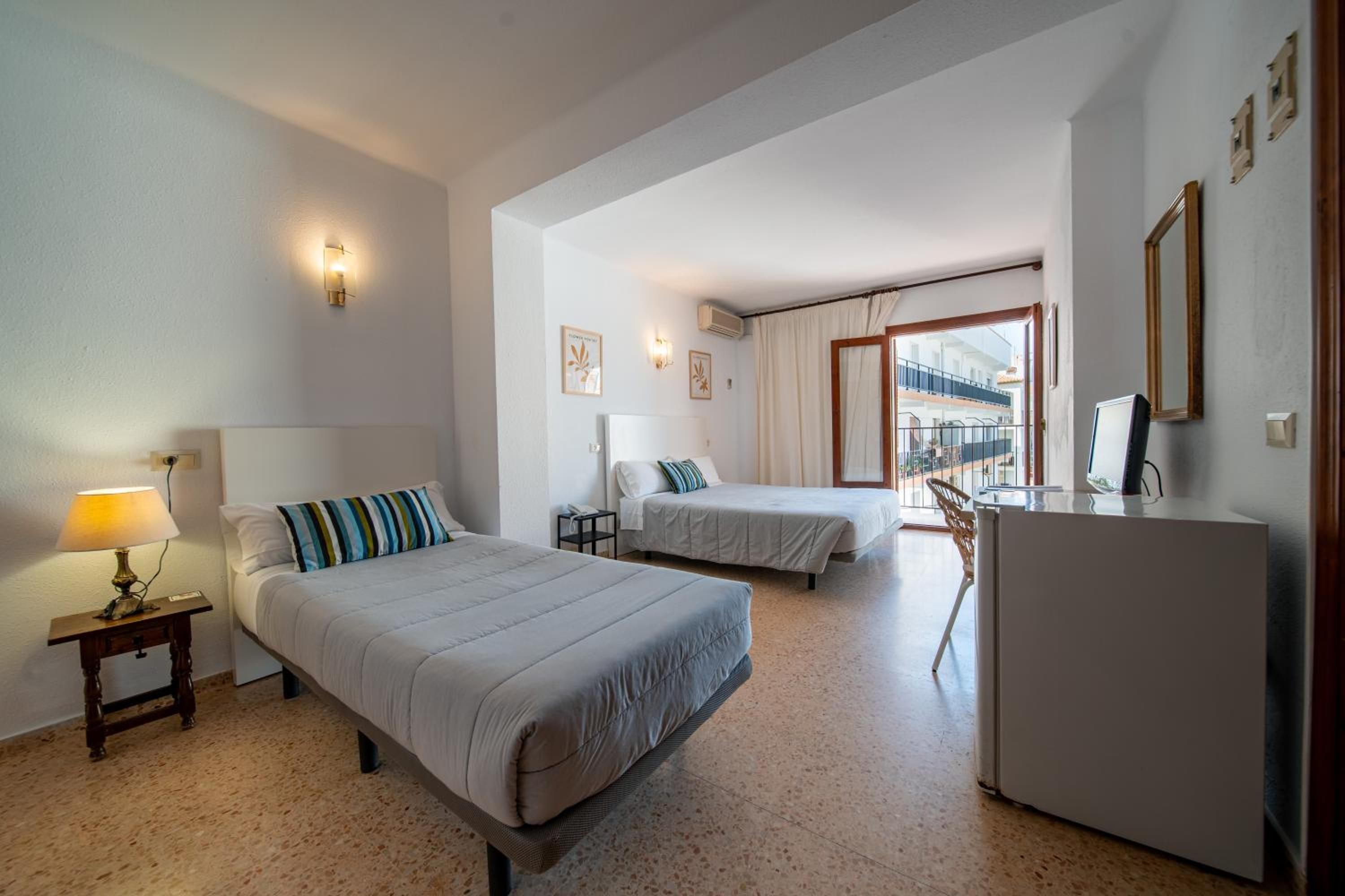 Habitación de hotel con dos camas, un escritorio, una lámpara y un refrigerador.