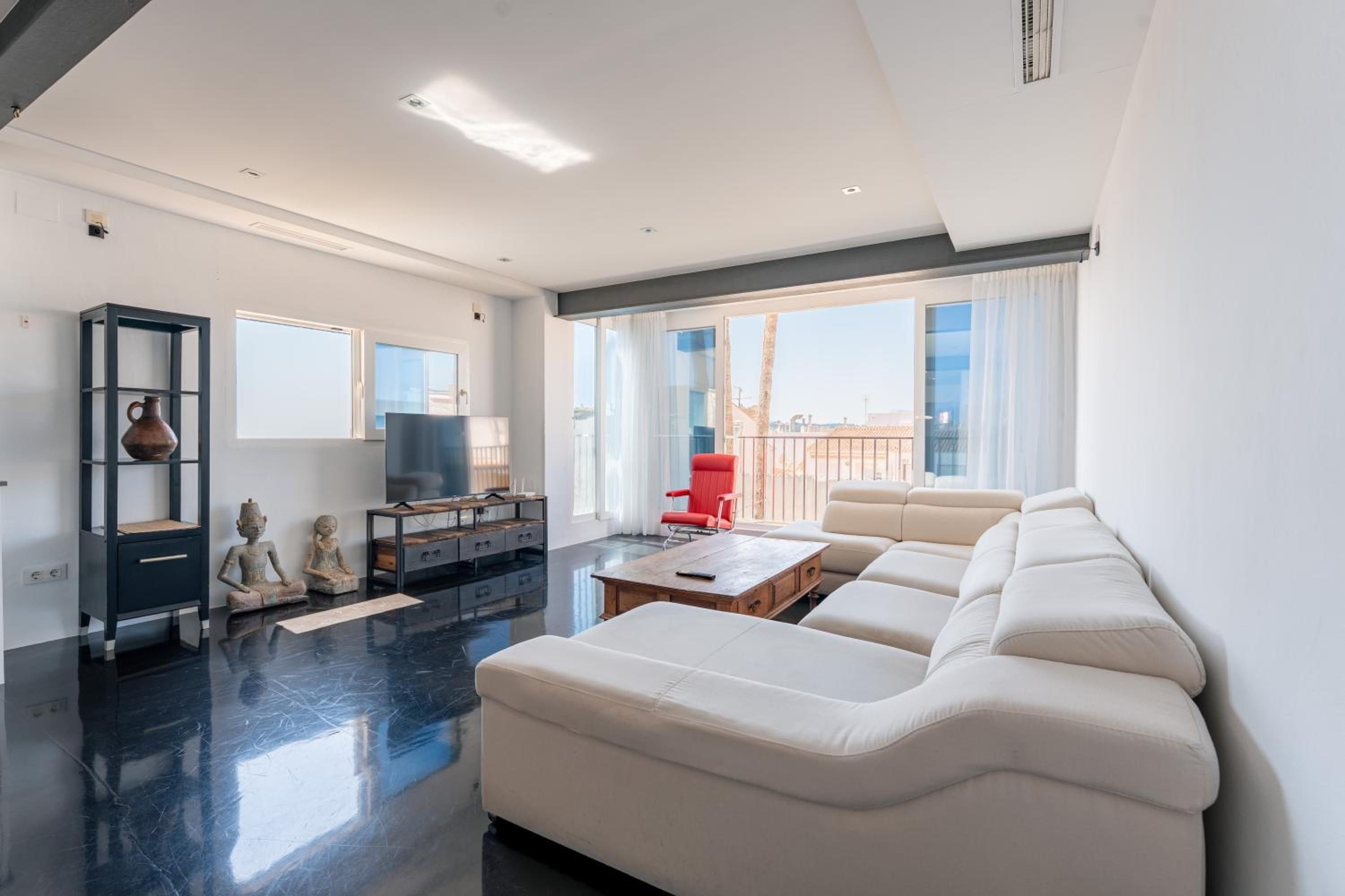 Una sala de estar moderna con un sofá, una silla roja, un televisor y una estantería decorativa.