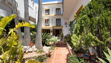 Un patio con un sendero adoquinado, plantas en macetas y un edificio con balcones.