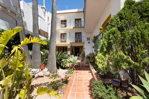 A courtyard with a tiled pathway, potted plants, and a building with balconies. - Hotel Buigues (Teulada)