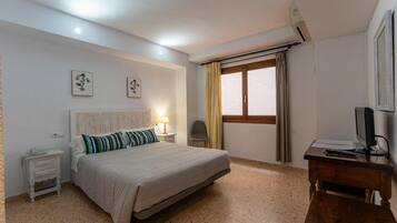 Habitación de hotel con cama, mesitas de noche, un escritorio con computadora, una silla, ventana con cortinas y decoración en la pared.
