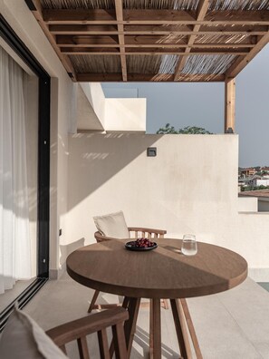 A round wooden table with a bowl of fruit and a glass of water, a wooden chair, and a ceiling with a wooden beam structure. - Seven Rocks Chalkidiki (Kassandra)