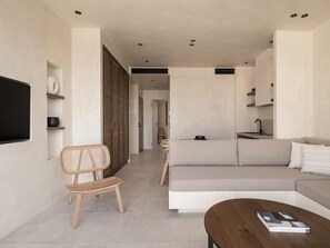 A modern living room with a sofa, a wooden chair, a coffee table, and a flat-screen TV mounted on the wall. - Seven Rocks Chalkidiki (Kassandra)