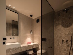 A modern bathroom with a large mirror, a built-in sink, a shower enclosure, and a toilet. - Seven Rocks Chalkidiki (Kassandra)