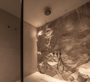 A modern shower with a textured wall, recessed lighting, and a handheld showerhead. - Seven Rocks Chalkidiki (Kassandra)