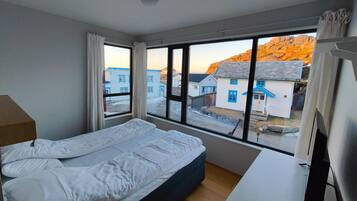 Un dormitorio con cama, escritorio y un ventanal con vistas a edificios y una montaña.