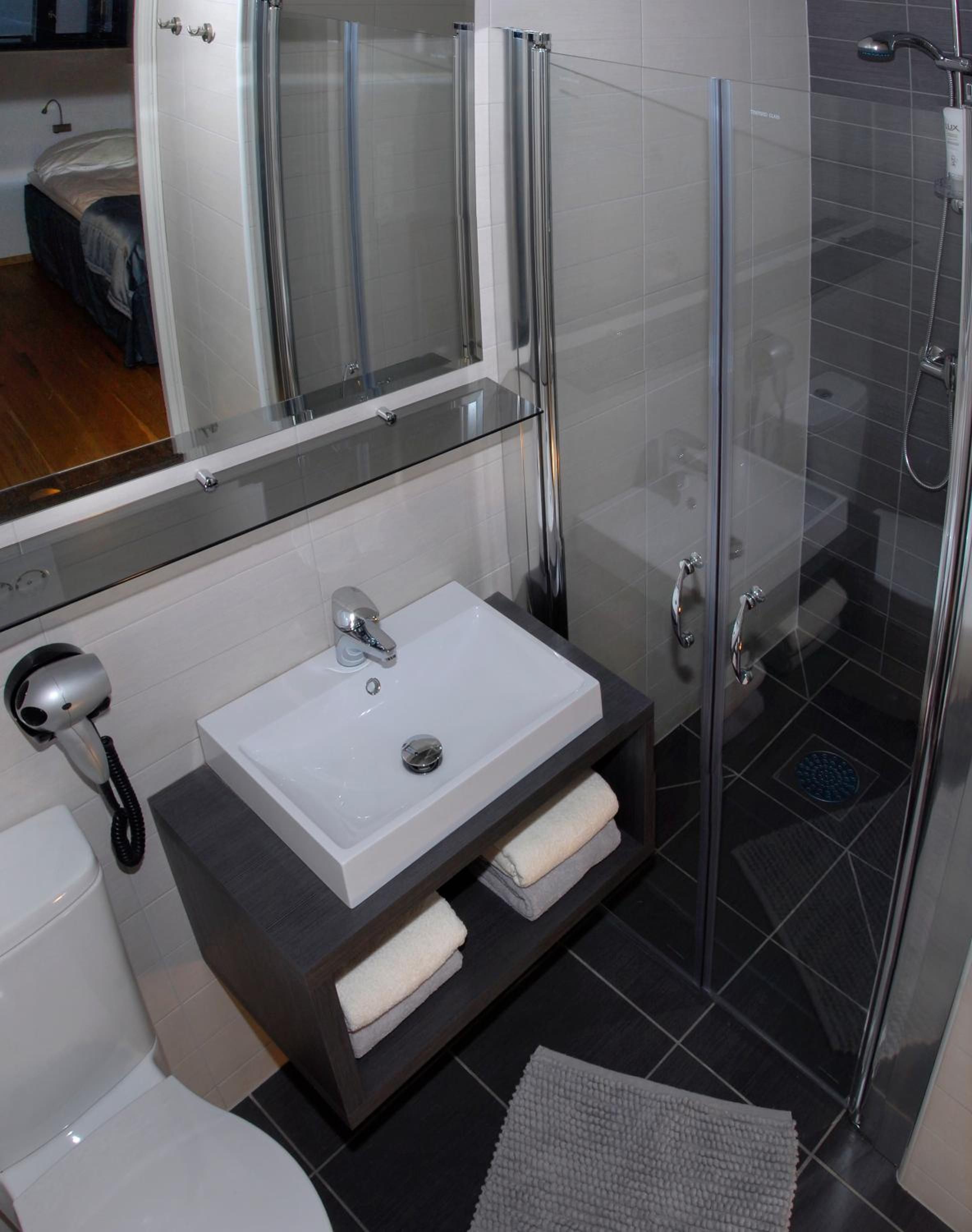 Un baño moderno con ducha de mampara de vidrio, lavabo blanco y tocador oscuro.