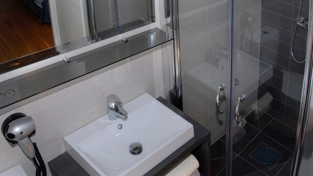Un baño moderno con ducha de mampara de vidrio, lavabo blanco y tocador oscuro.