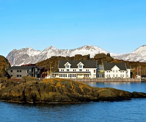 A coastal building with a dock, surrounded by rocky terrain and snow-capped mountains.