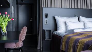 A modern hotel room with a bed, a desk with a chair, and a vase of flowers.