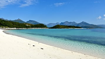 A beach with clear turquoise water, white sand, and a forested island with mountains in the background.