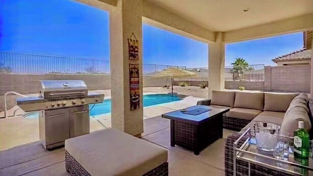 Ein überdachter Außenbereich mit Pool, Grill und einer Sitzecke mit Tisch und Kissen.