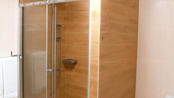 A modern bathroom with a glass-enclosed shower, wooden paneling, a white sink, and a toilet.