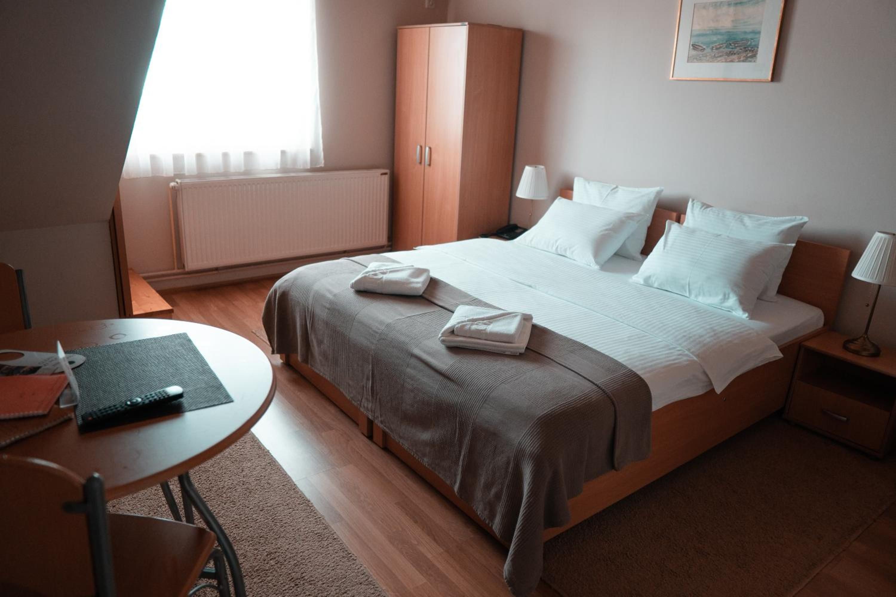 A hotel room with a bed, bedside tables, a desk, and a radiator.