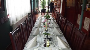 A long dining table set with multiple chairs, a vase of flowers, and a bottle of champagne. - Hotel Topcider (Belgrade)