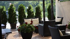 A covered outdoor seating area with wicker furniture, potted plants, and a view of the surrounding greenery. - Hotel Topcider (Belgrade)