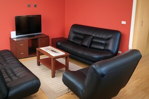 Una sala de estar con un sofá, una mesa de centro, un televisor en un mueble bajo y un aparador de madera.
