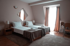 A hotel room with two beds, a sitting area, a window with curtains, and a mirror on the wall. - Hotel Topcider (Belgrade)
