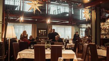 An indoor dining area with tables set for guests, overhead lighting, and a view of the outdoors through large windows.