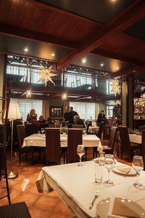 An indoor dining area with tables set for guests, overhead lighting, and a view of the outdoors through large windows. - Hotel Topcider (Belgrade)