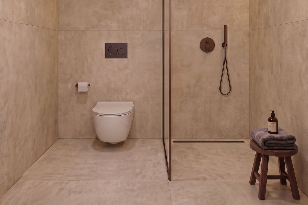 Un baño moderno con ducha, inodoro y un taburete pequeño con toallas.