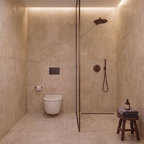 A modern bathroom with a shower, toilet, and a small stool with towels. - Breaq Santorini Hotel (Santorini)