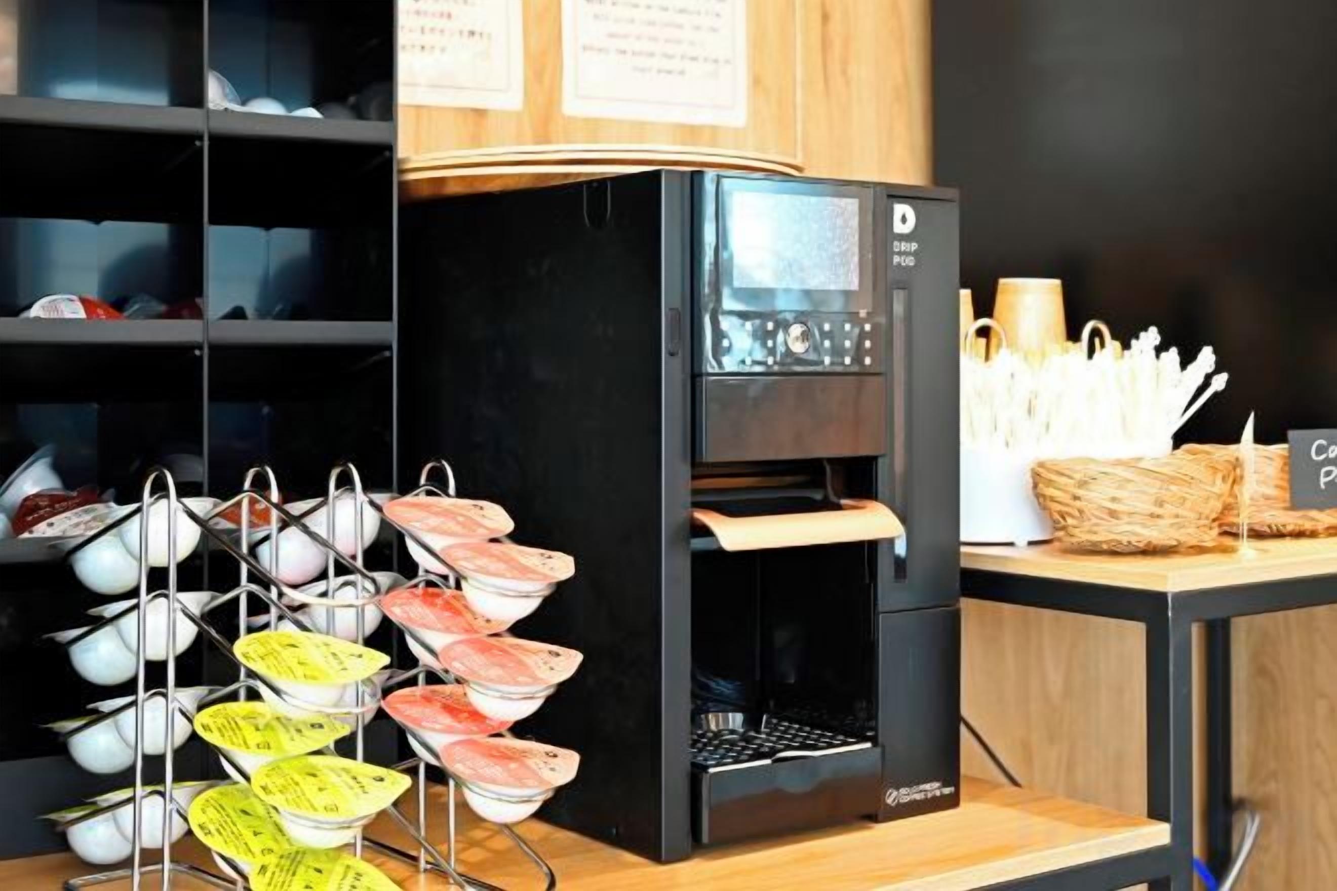 Máquina de café com tela, espaço para café com copos descartáveis e cesta de utensílios.