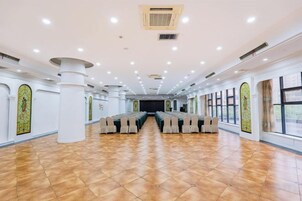 Un salón amplio con filas de sillas, un escenario y ventanas grandes.