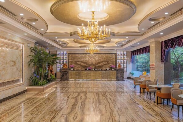 Un vestíbulo con piso de mármol, un candelabro, una recepción y zonas de estar.