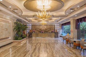 Un vestíbulo con piso de mármol, un candelabro, una recepción y zonas de estar.