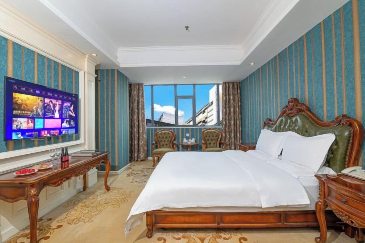 A hotel room with a large bed, a television, a desk, and a view of the mountains.