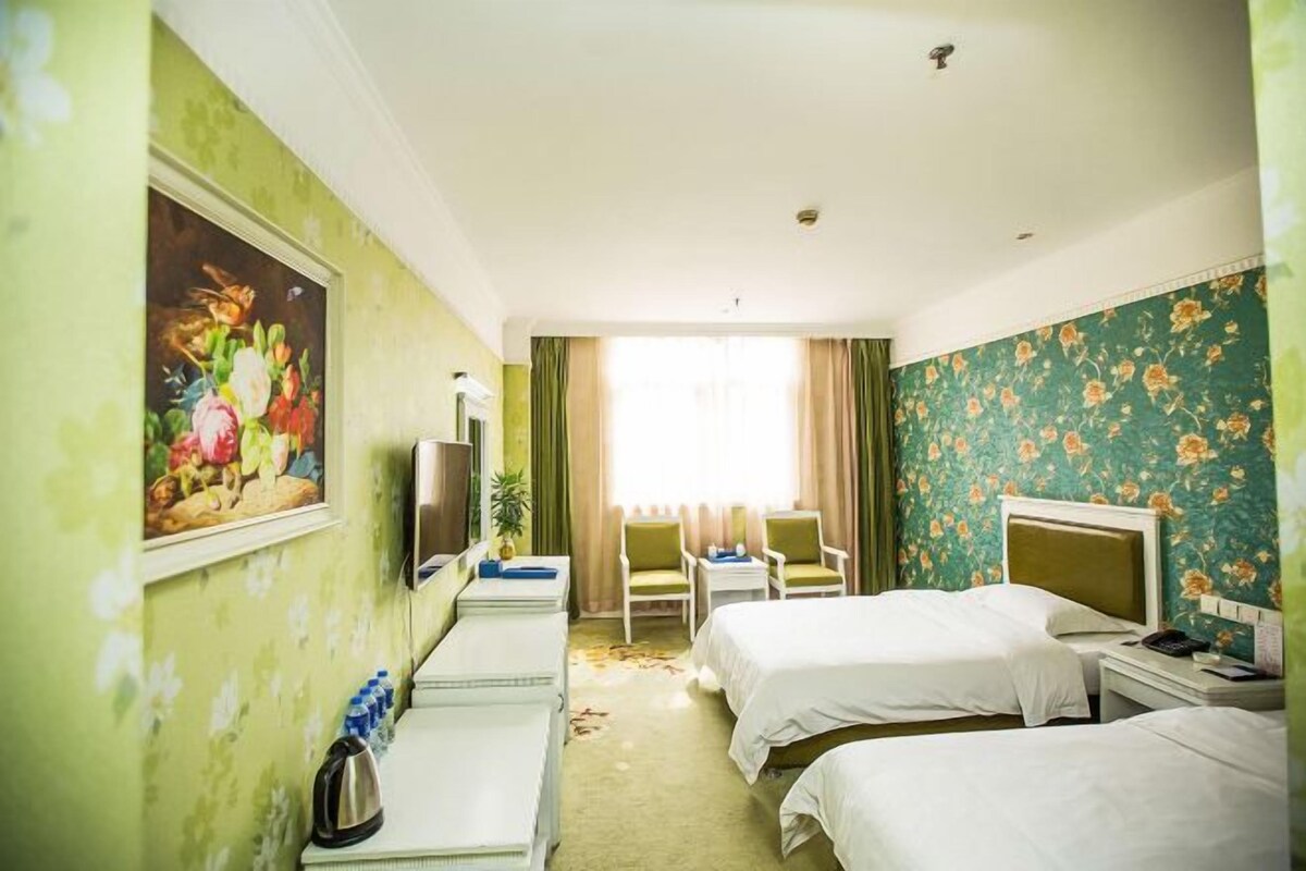 Habitación de hotel con dos camas, un escritorio, una silla, un televisor y un cuadro en la pared.