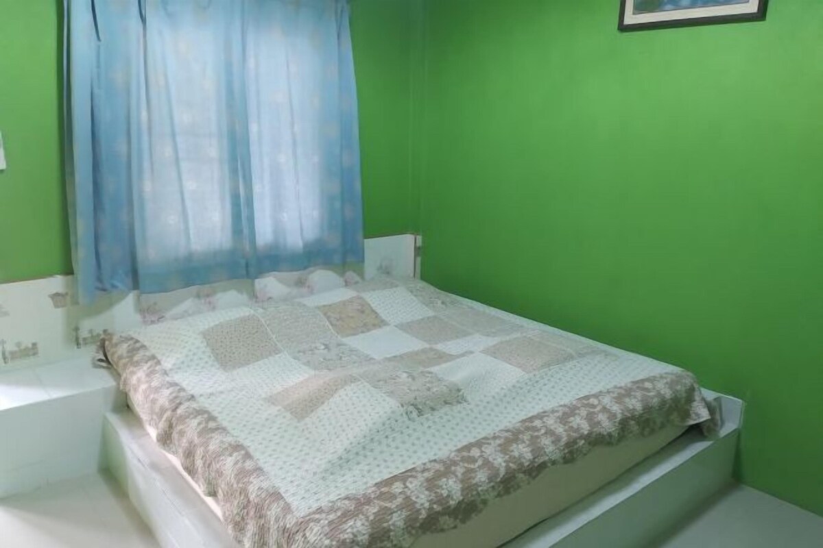 A bed with a quilt, a window with a blue curtain, and a green wall.