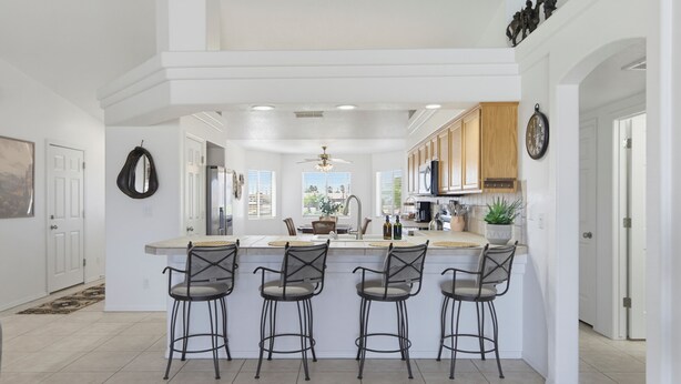 A modern kitchen with a central island, bar stools, wooden cabinets, and a large window. - Desert Horizon Retreat - Pool, Spa & Desert Views (Lake Havasu City)
