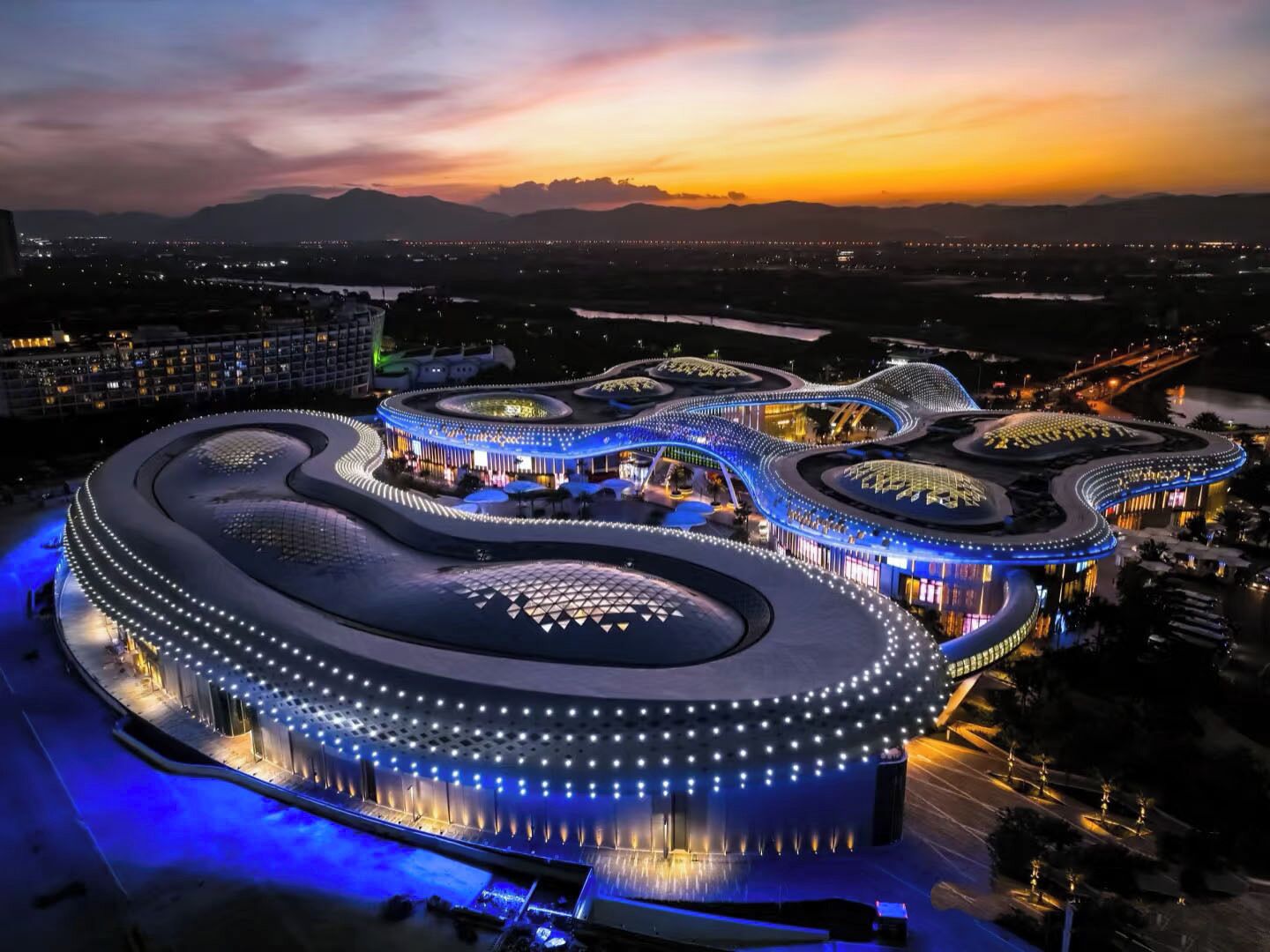A modern, circular building with a unique architectural design, surrounded by a well-lit area.