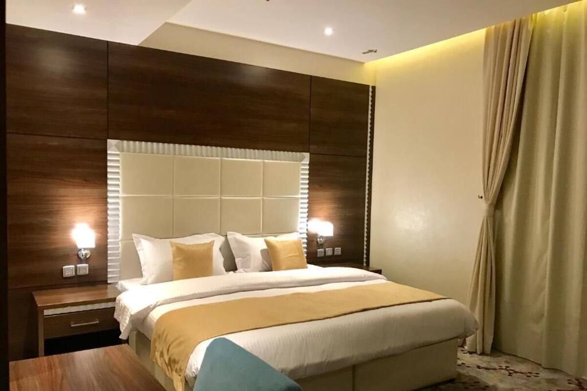 A hotel room with a large bed, a wooden nightstand, a desk, and a window with curtains.