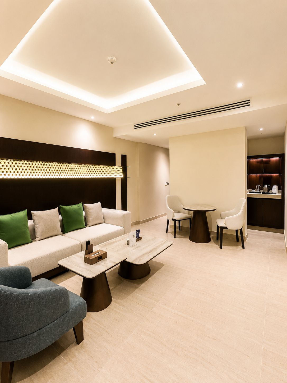 Una habitación de hotel moderna con sofá, sillones, una mesa de comedor y una zona de cocina.