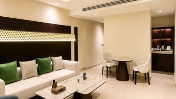 Una habitación de hotel moderna con sofá, sillones, una mesa de comedor y una zona de cocina.