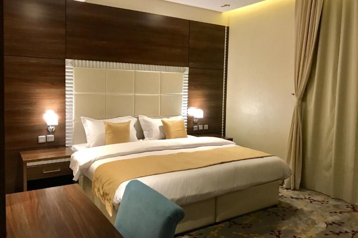 Una habitación de hotel con una cama grande, una mesita de noche de madera, un escritorio y una ventana con cortinas.