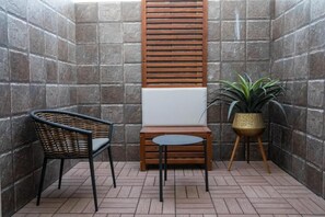 Un pequeño patio amurallado con pared de piedra, separador de madera, una silla de mimbre, una mesita redonda y una planta en maceta.