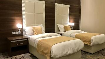 Habitación de hotel con dos camas, cabecero de madera, mesita de noche y alfombra estampada.