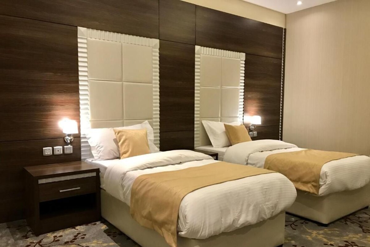 A hotel room with two beds, a wooden headboard, a nightstand, and a patterned carpet.