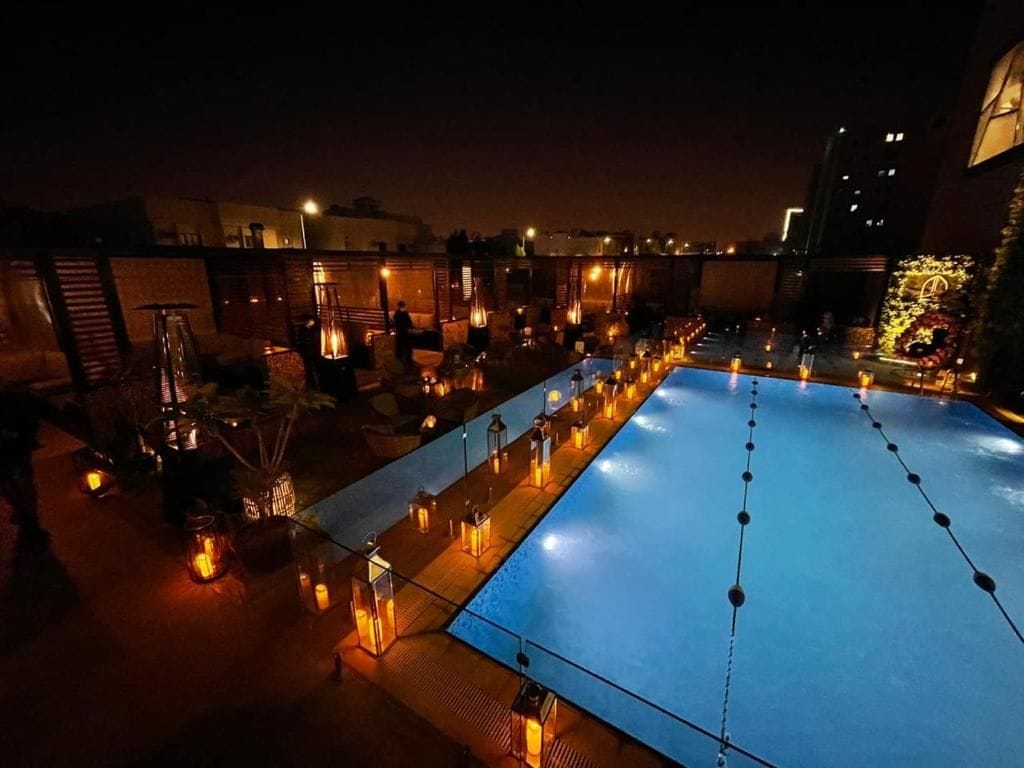 Un área de piscina en la azotea con una piscina azul, rodeada de faroles y plantas en macetas.