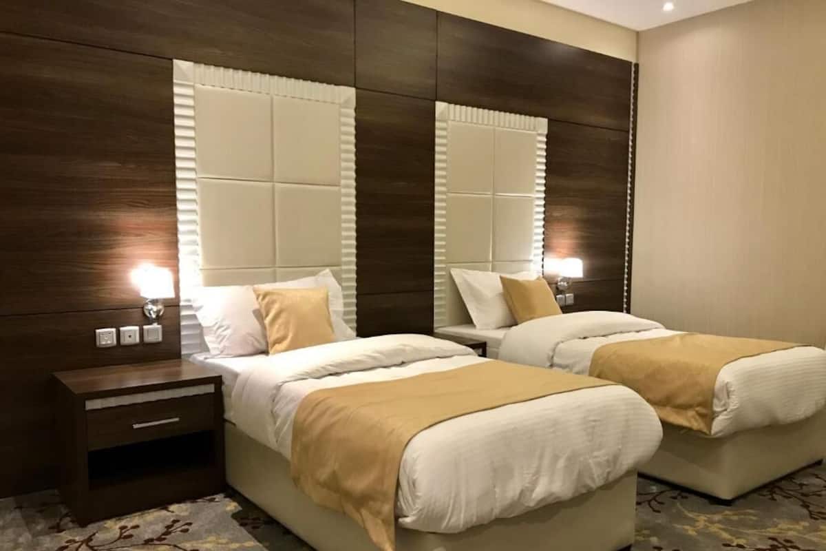 A hotel room with two beds, a wooden headboard, a nightstand, and a patterned carpet.