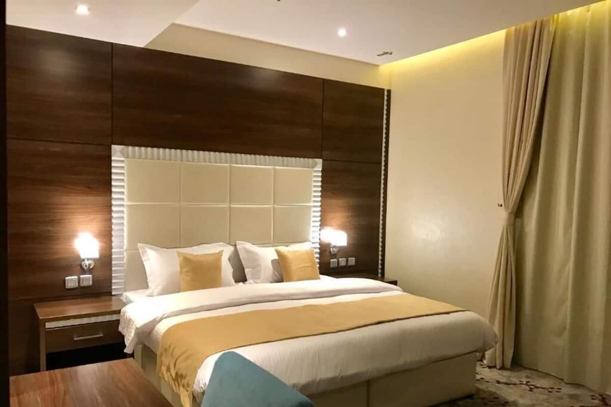 A hotel room with a large bed, a wooden nightstand, a desk, and a window with curtains.