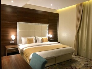 Una habitación de hotel con una cama grande, una mesita de noche de madera, un escritorio y una ventana con cortinas.