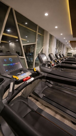 Vários equipamentos de corrida em uma academia, com um painel de controle no primeiro esteira.