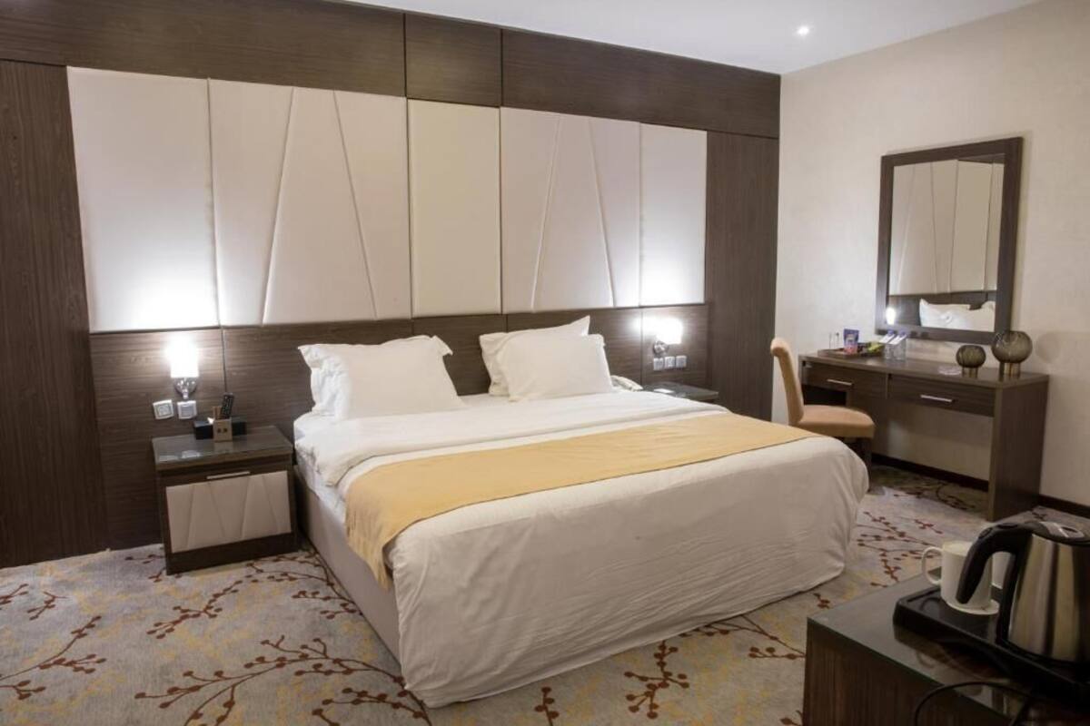 A hotel room with a large bed, bedside tables, a dresser, a mirror, and a coffee maker.
