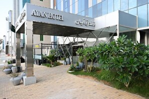 Exterior do Hotel Ayan com design arquitetônico moderno, apresentando uma entrada coberta e plantas em vasos.