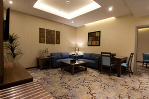 Habitación de hotel con sala de estar que incluye un sofá, una mesa de centro, un televisor y una planta decorativa.